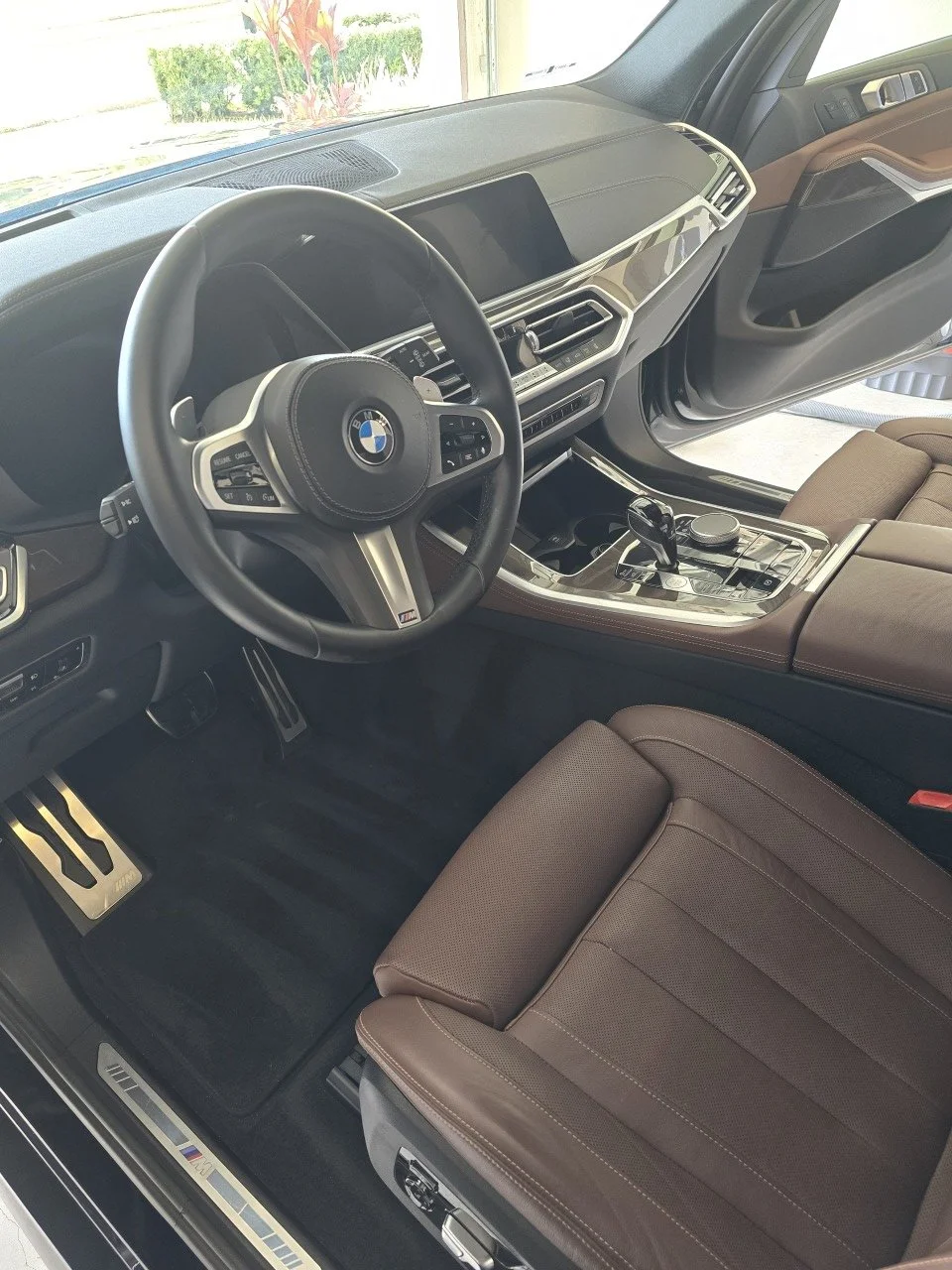 Interior of a BMW vehicle showing the steering wheel, dashboard, center console, and brown front seat cleaned by wash boss.