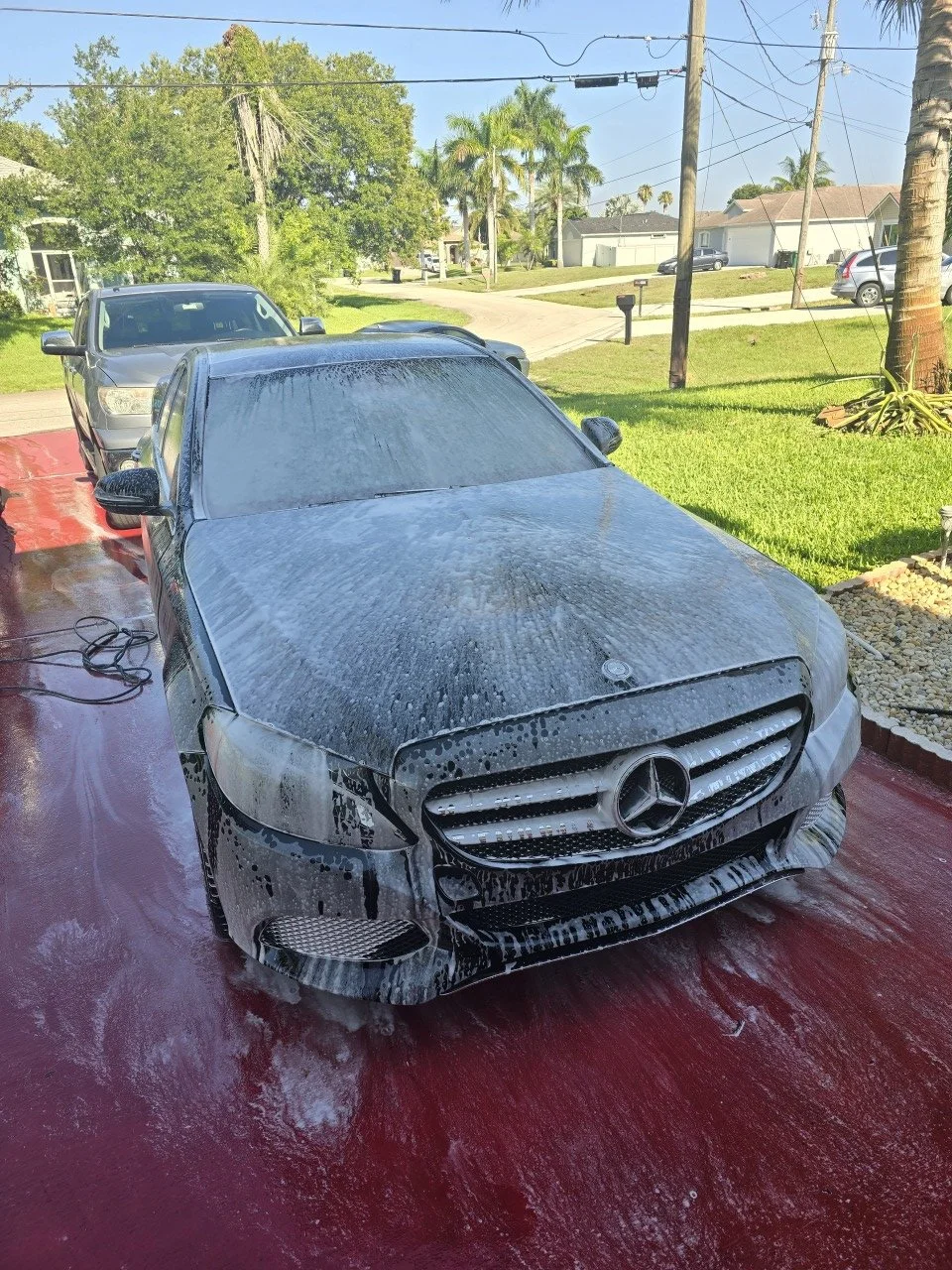 A gray Mercedes-Benz being washed with soap and foam on a red driveway, by wash boss mobile detailing