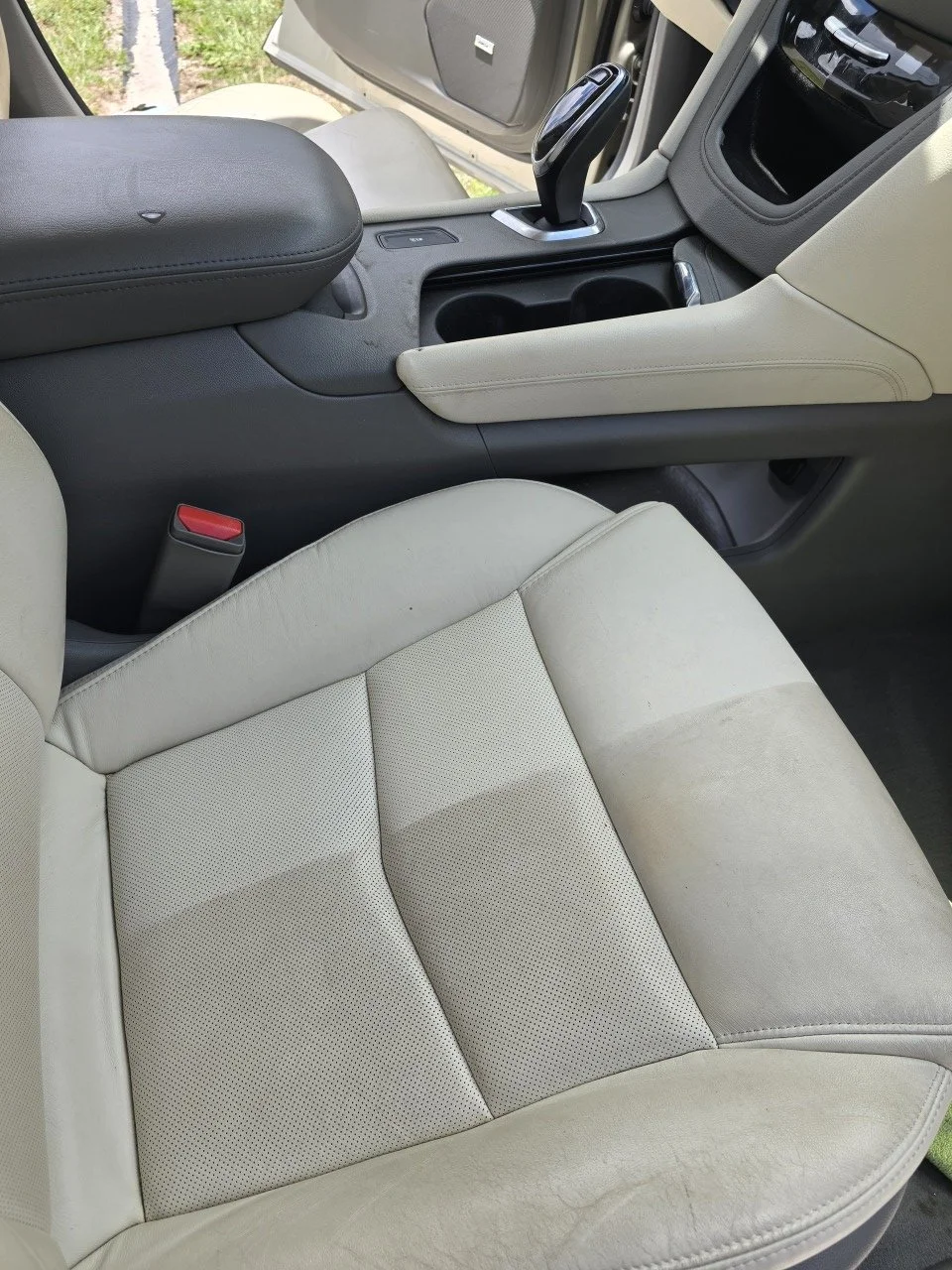 The interior of a vehicle showing a beige leather driver's seat, center console with gear shifter, and dashboard detail.