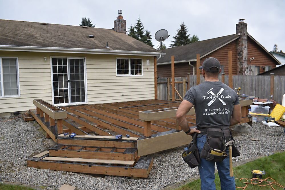 Tool & Trade carpenter framing a new deck behind a home