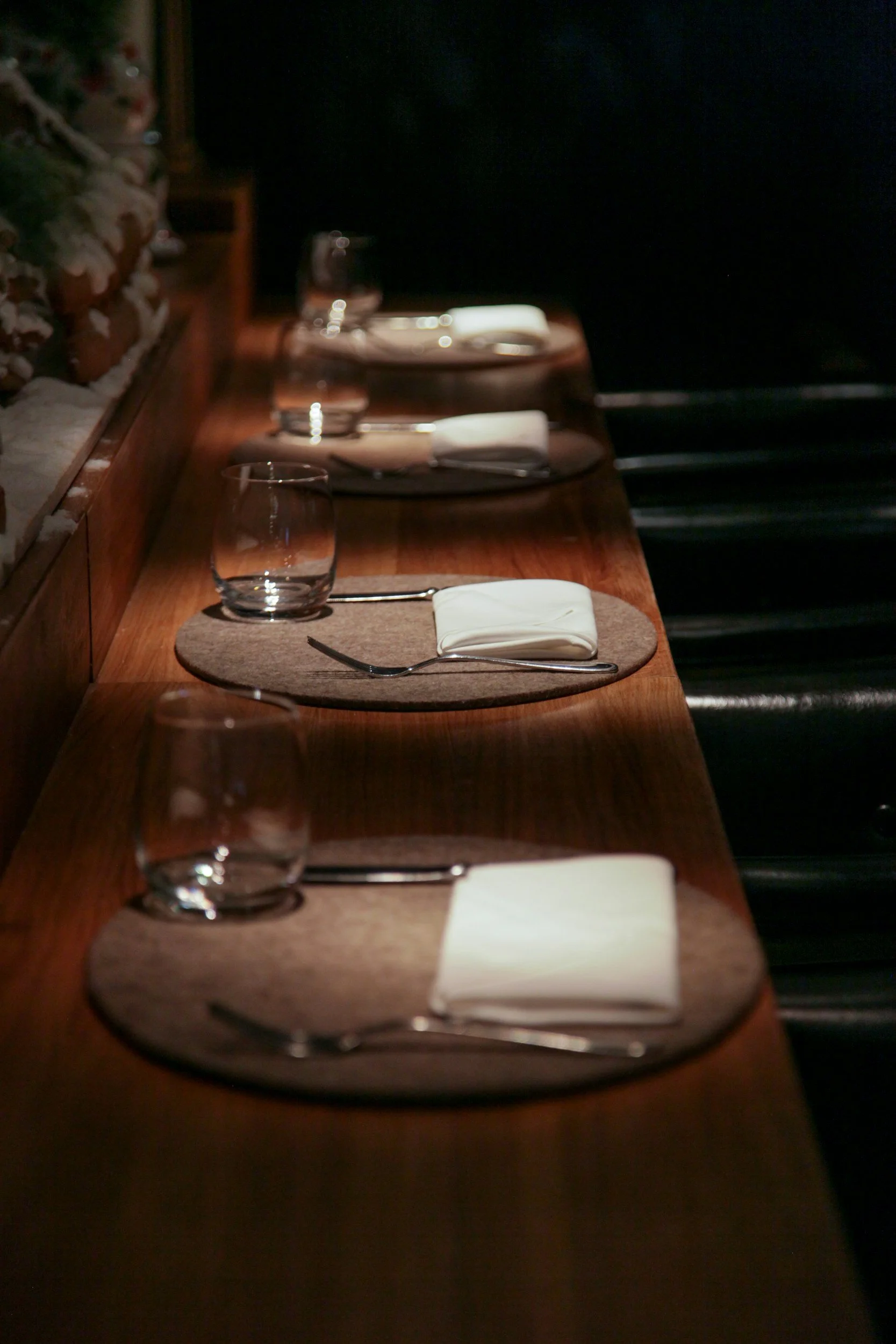 Minimalist bar seating with neatly arranged place settings, glassware, and folded napkins, highlighting an intimate chef’s counter dining experience