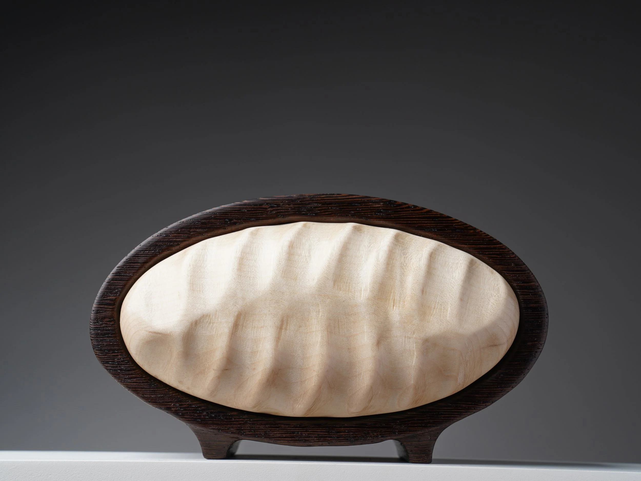 Oval wenge bandsaw box with a pale curly maple drawer front carved in flowing waves.
