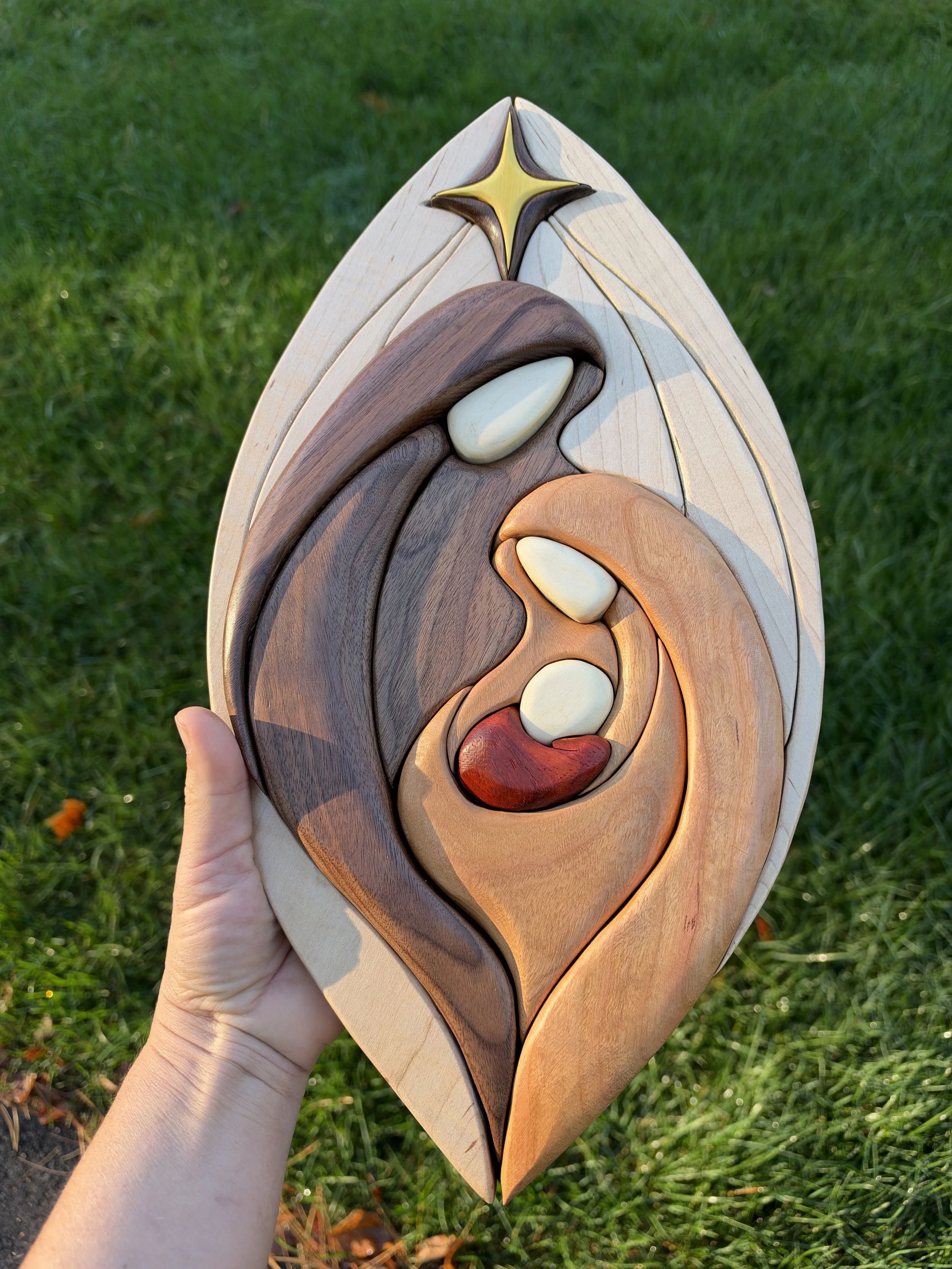 Handmade wooden nativity wall hanging photographed against greenery