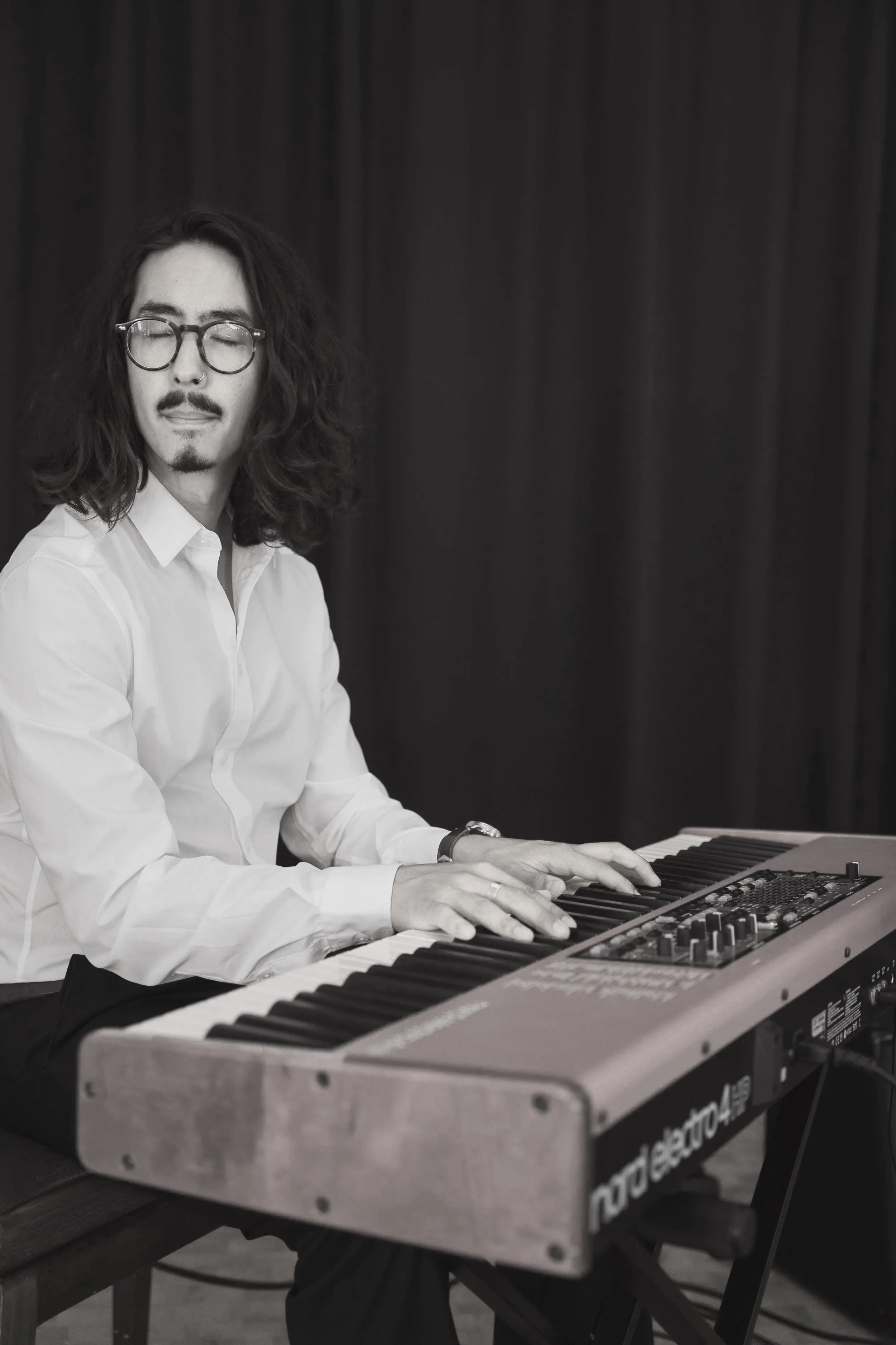 Ein Mann spielt Trompete neben einem Musiker an einem Keyboard, umgeben von einer Gruppe elegant gekleideter Menschen, möglicherweise auf einer Hochzeitsfeier oder einem Event im Freien.