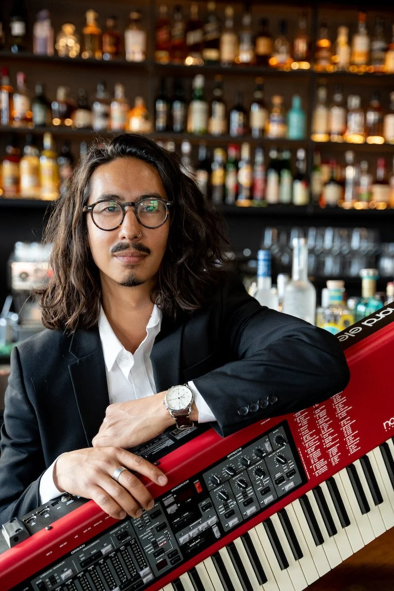 Ein Mann mit Brille und dunklen, wallenden Haaren spielt auf einer roten Tastatur, im Hintergrund eine Wand voller Flaschen an der Bar im Restaurant Newport in Lübeck.