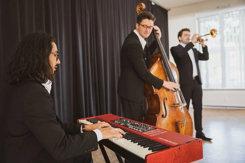 Musiker am Klavier, Kontrabass und Trompete vor einem schwarzen Bühnenvorhang.