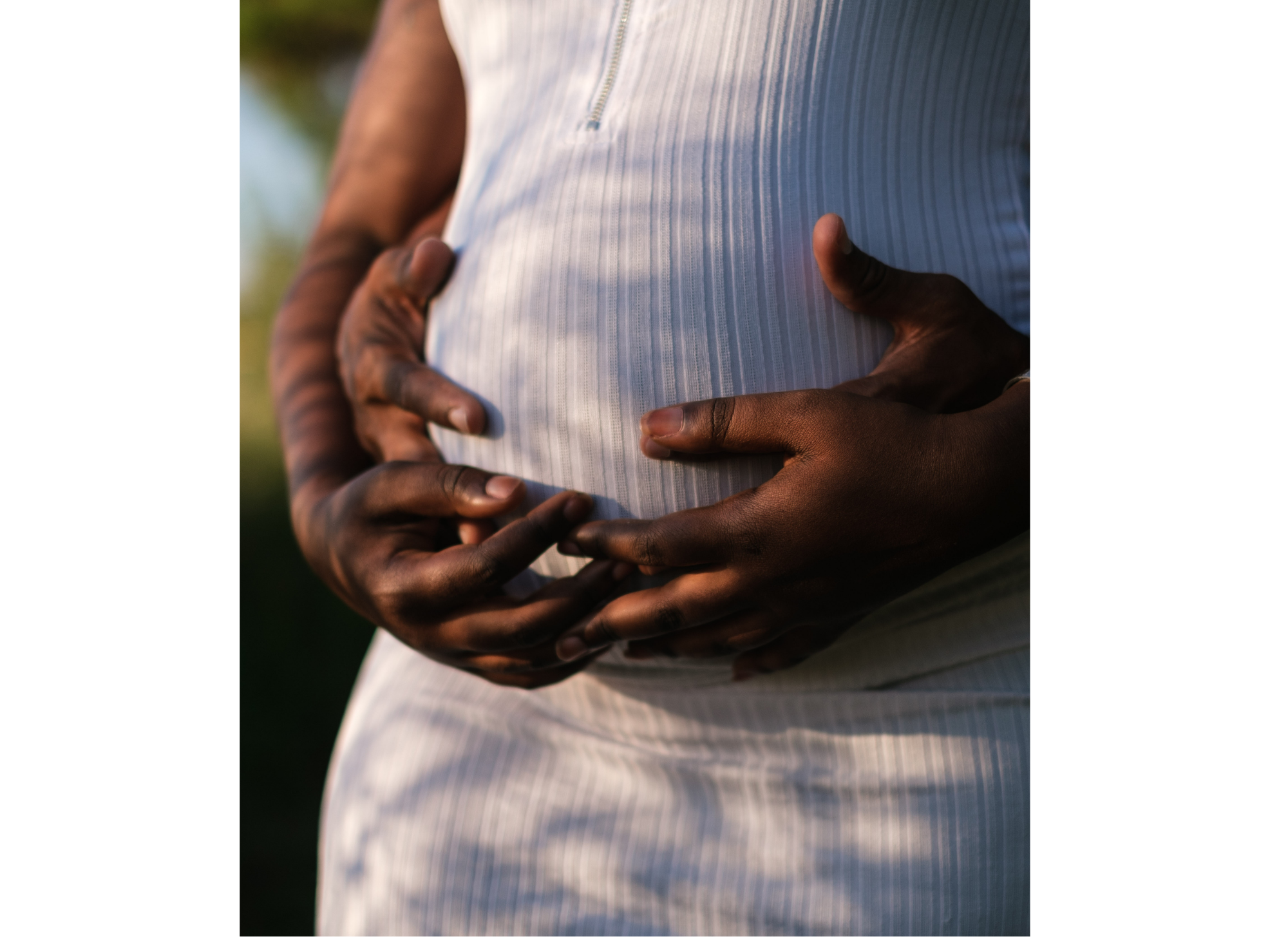 Woman holding her pregnant belly with her husbands hands wrapped around her.
