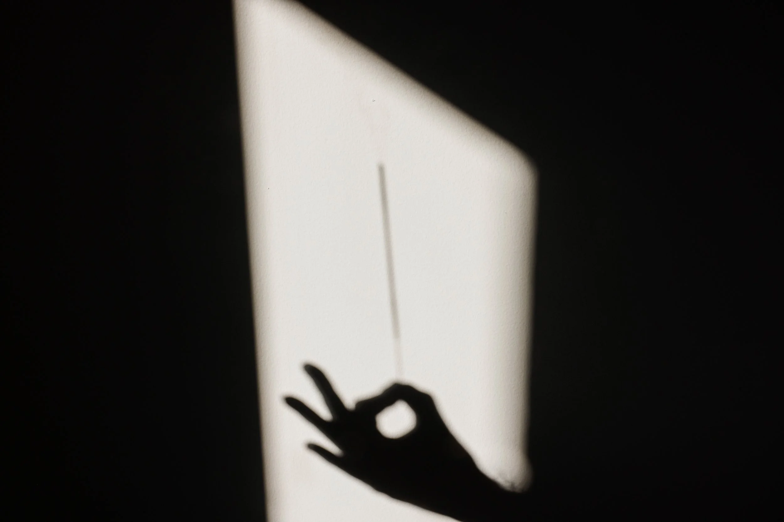 Shadow of a hand reaching towards a clock face with Roman numerals, with a shadow of a clock hand on the white background.