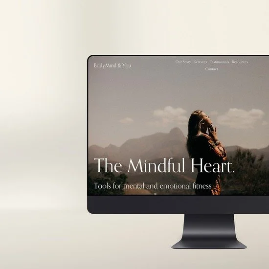 Computer monitor displaying a website titled "The Mindful Heart" with a woman practicing mindfulness outdoors and a mountain landscape background.
