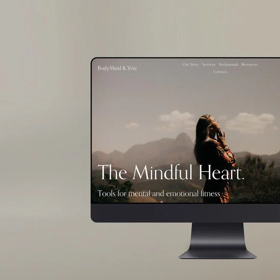 Computer monitor displaying a website titled "The Mindful Heart" with a woman in profile outdoors, mountain scenery in the background.