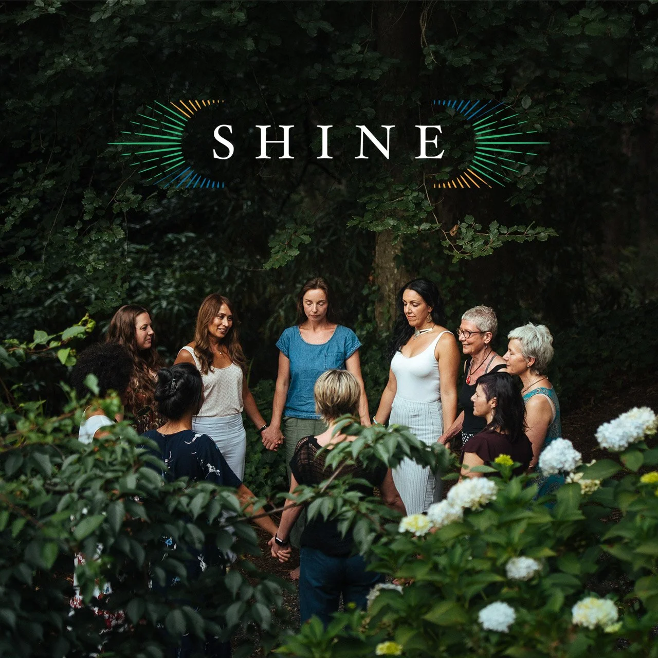 Group of women holding hands and standing in a circle outdoors surrounded by lush green foliage and white flowers, with the word 'SHINE' and colorful sound wave graphics above them.