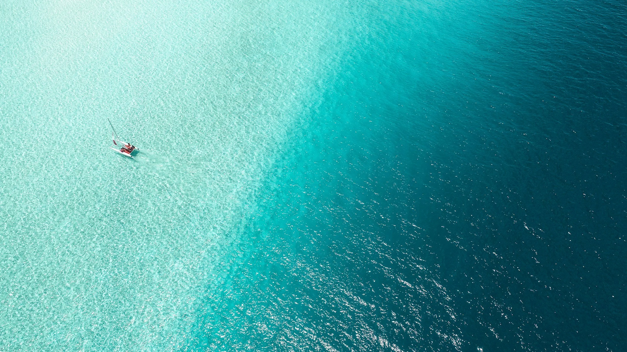 A sailboat sailing in clear turquoise and dark blue ocean waters.