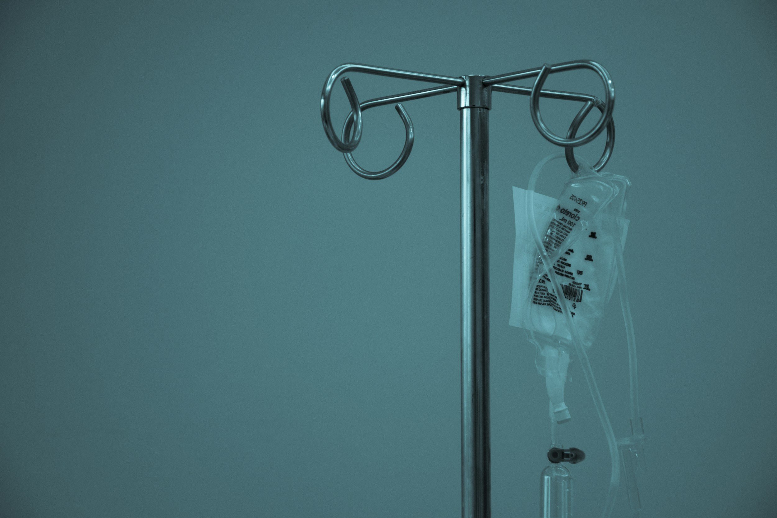 Medical IV drip stand with a hanging IV bag and tubing against a plain background.