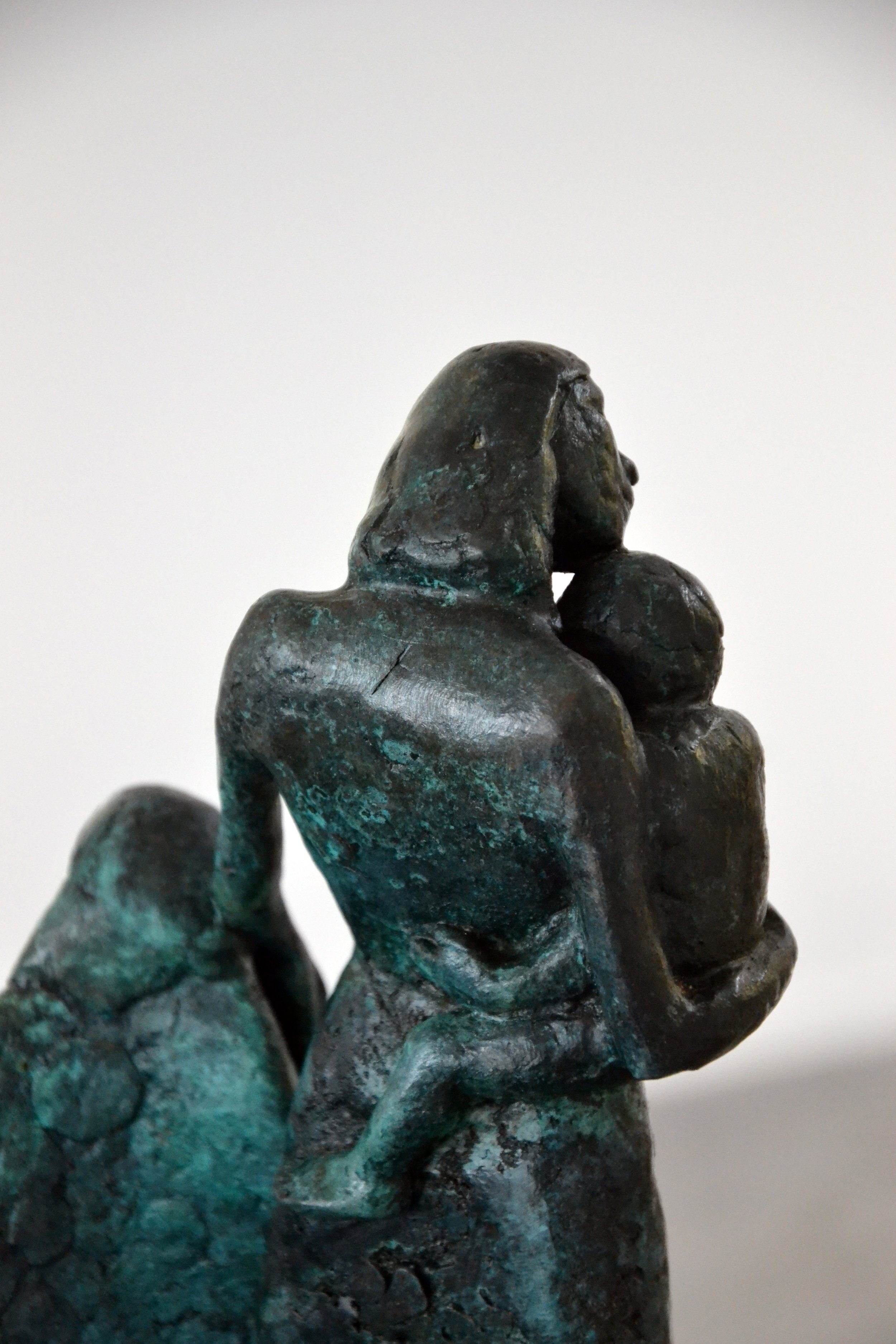 Bronze sculpture of a woman holding a child close to her face, with another figure partially visible in the background.