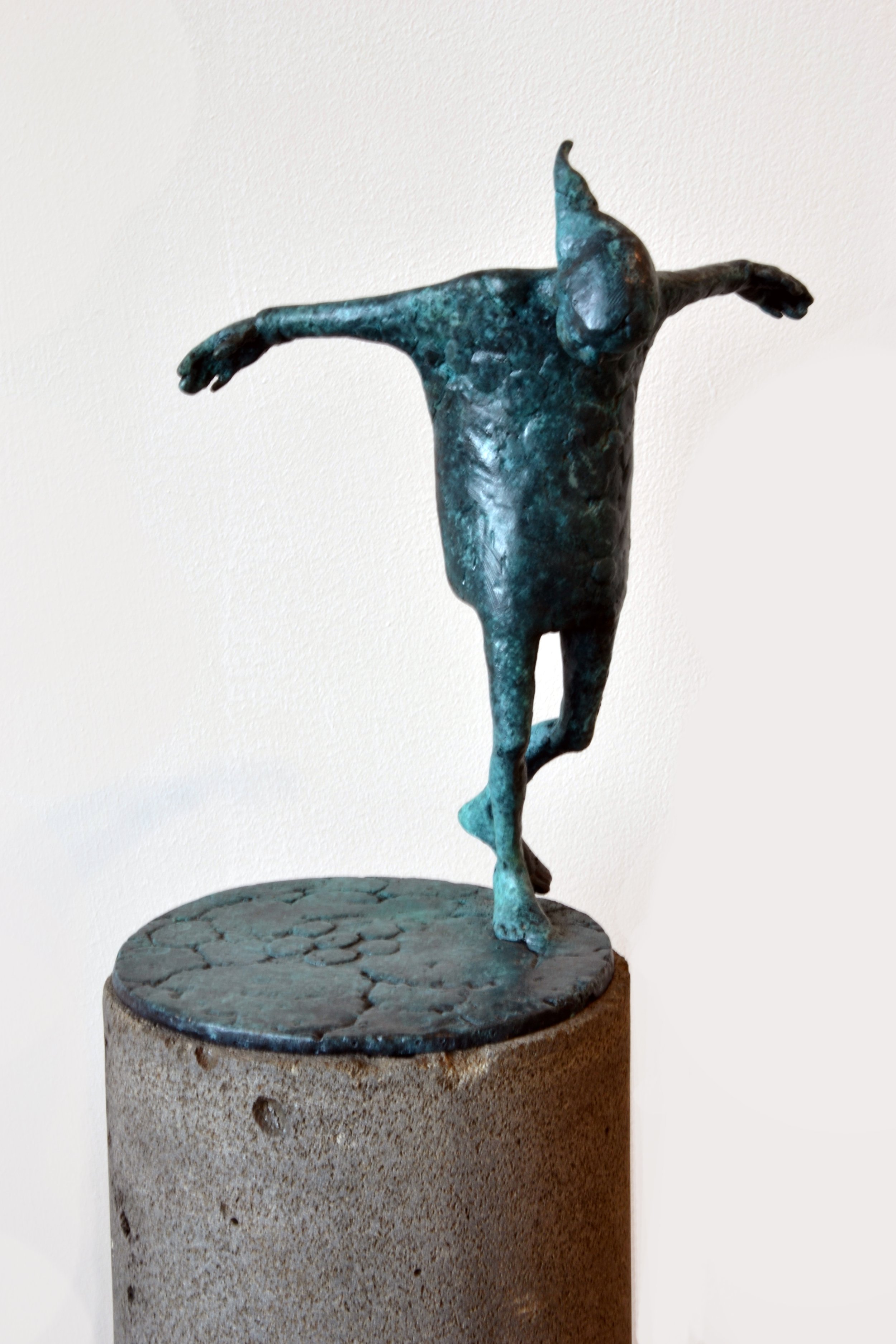 Bronze sculpture of a human figure with arms outstretched and head tilted back, mounted on a stone pedestal.