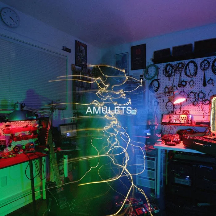 Colorful electronics and musical equipment in a room with text that reads 'Amulets,' and light streaks creating a dynamic effect.