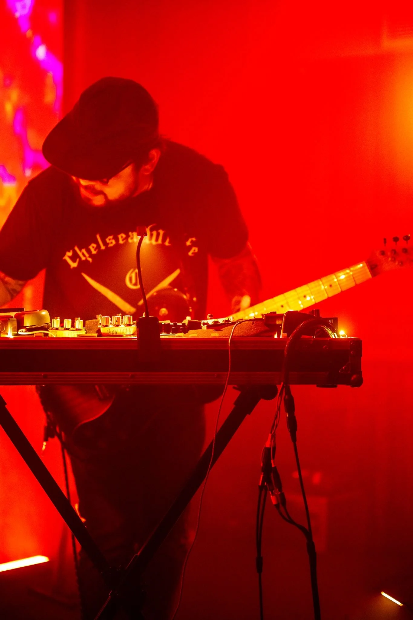 A person wearing a black hat and black playing guitar in a deep red lit show.