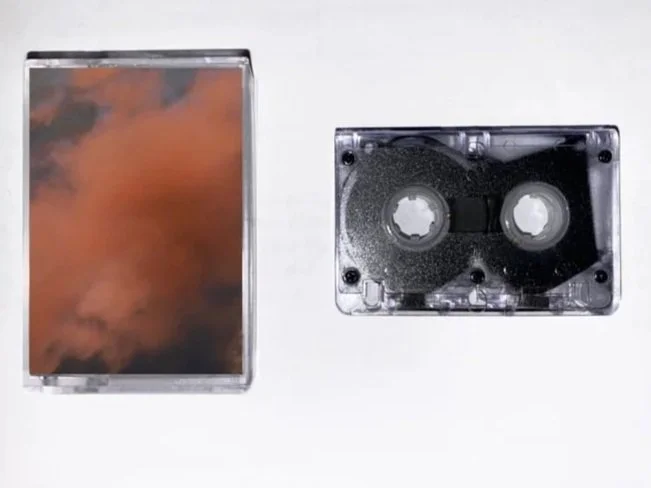 A cassette tape and a clear plastic case with a cloudy sky image inside.