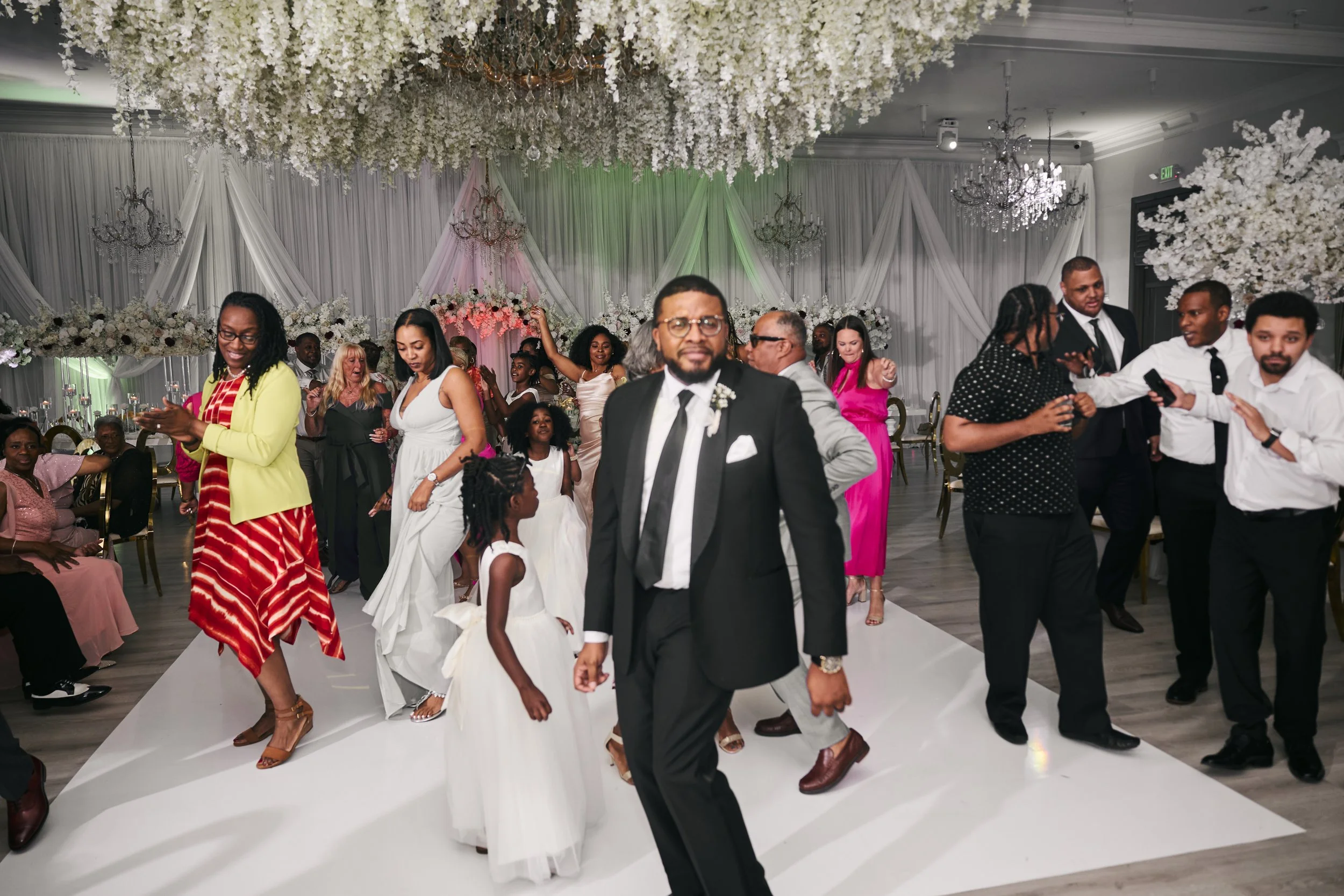 People dancing and socializing at a decorated wedding reception with floral and chandelier decorations.