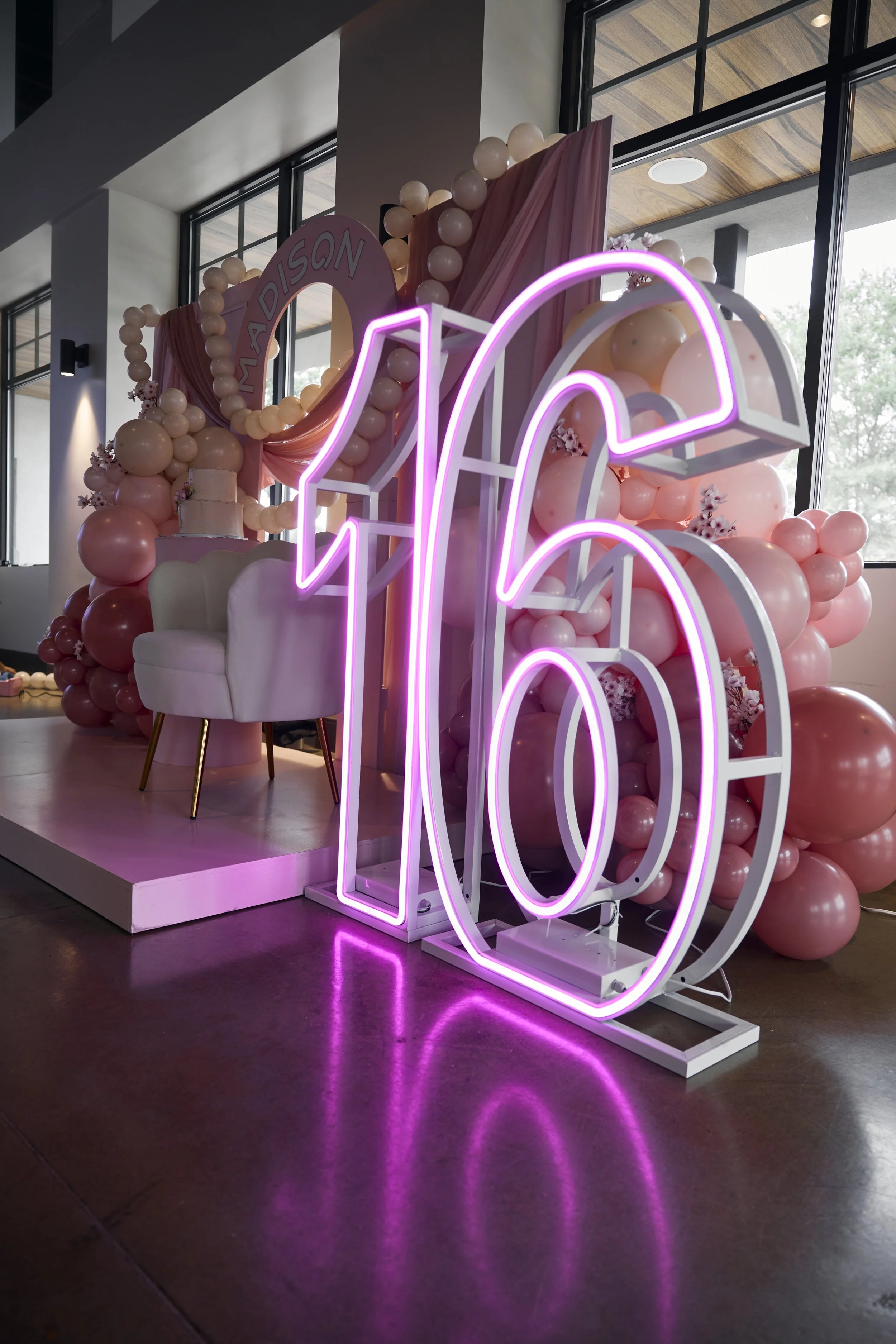 Large neon pink number 16 sign in front of pink balloon and cloth decoration for a Sweet 16 birthday celebration.