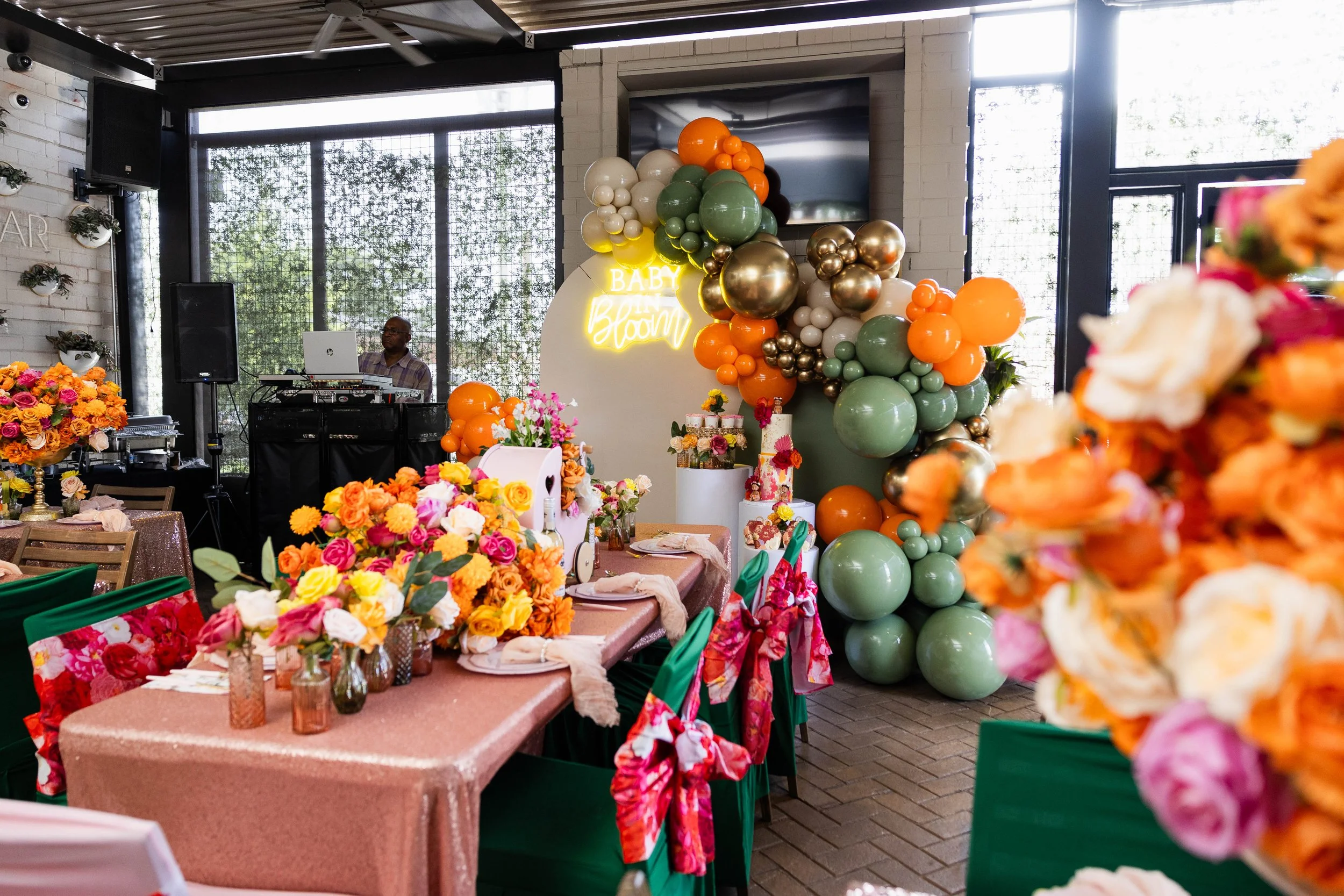 Decorated party room with colorful flowers, balloons, and a DJ setup, likely for a celebration such as a baby shower.
