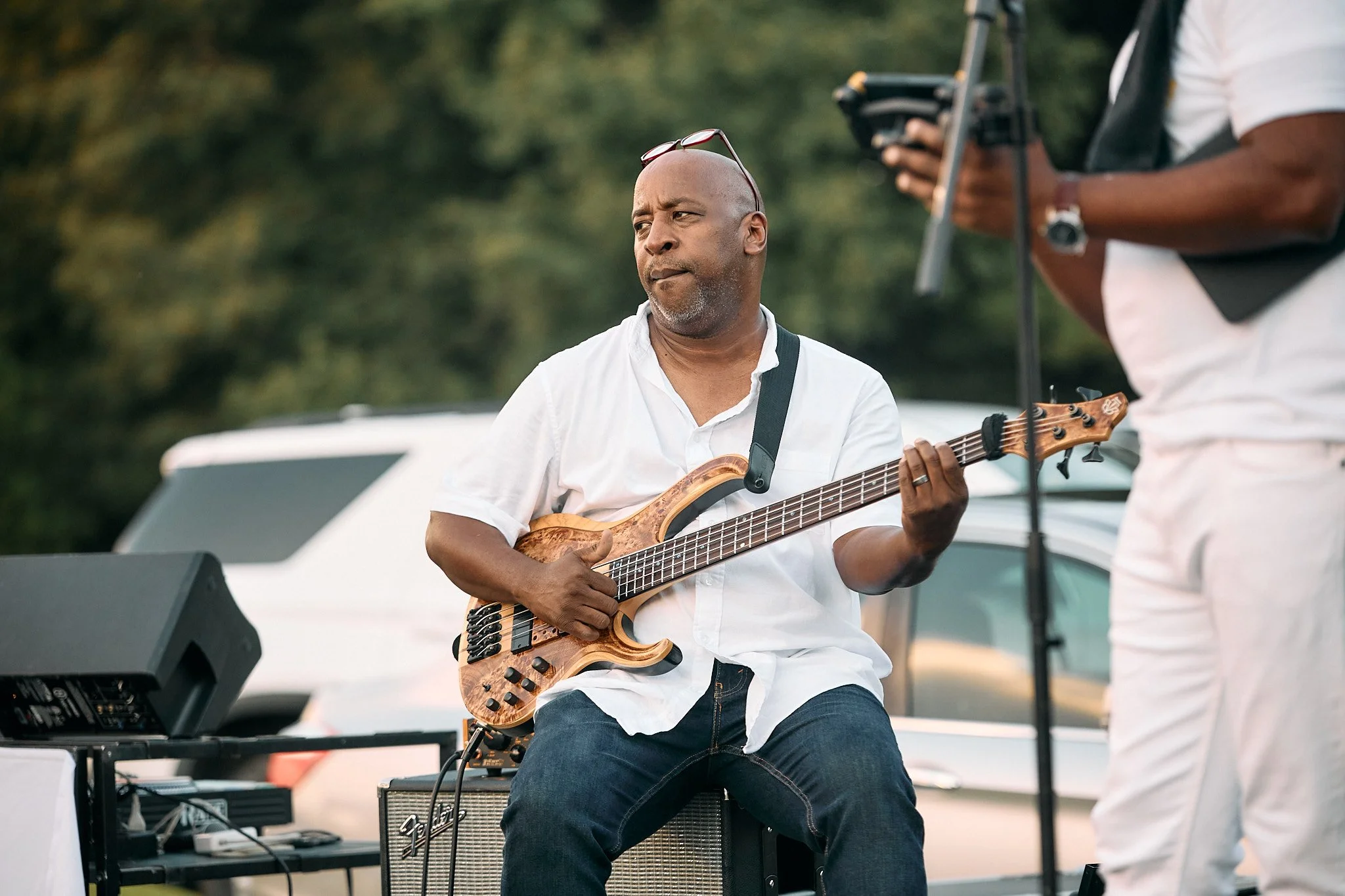 A man playing an electric bass guitar during an outdoor performance.