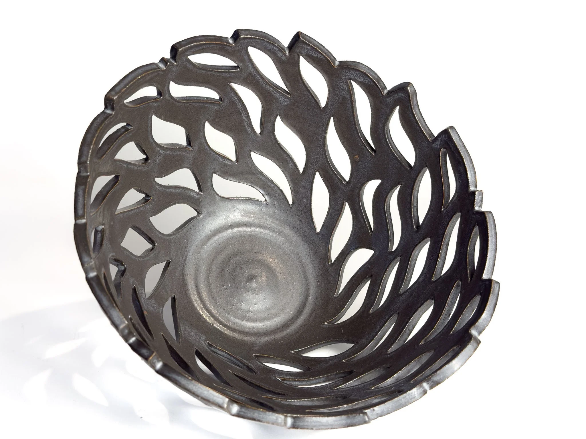 Close-up of a black, intricately designed metal circular object with cut-out patterns resembling hair or feathers, placed against a stark white background.