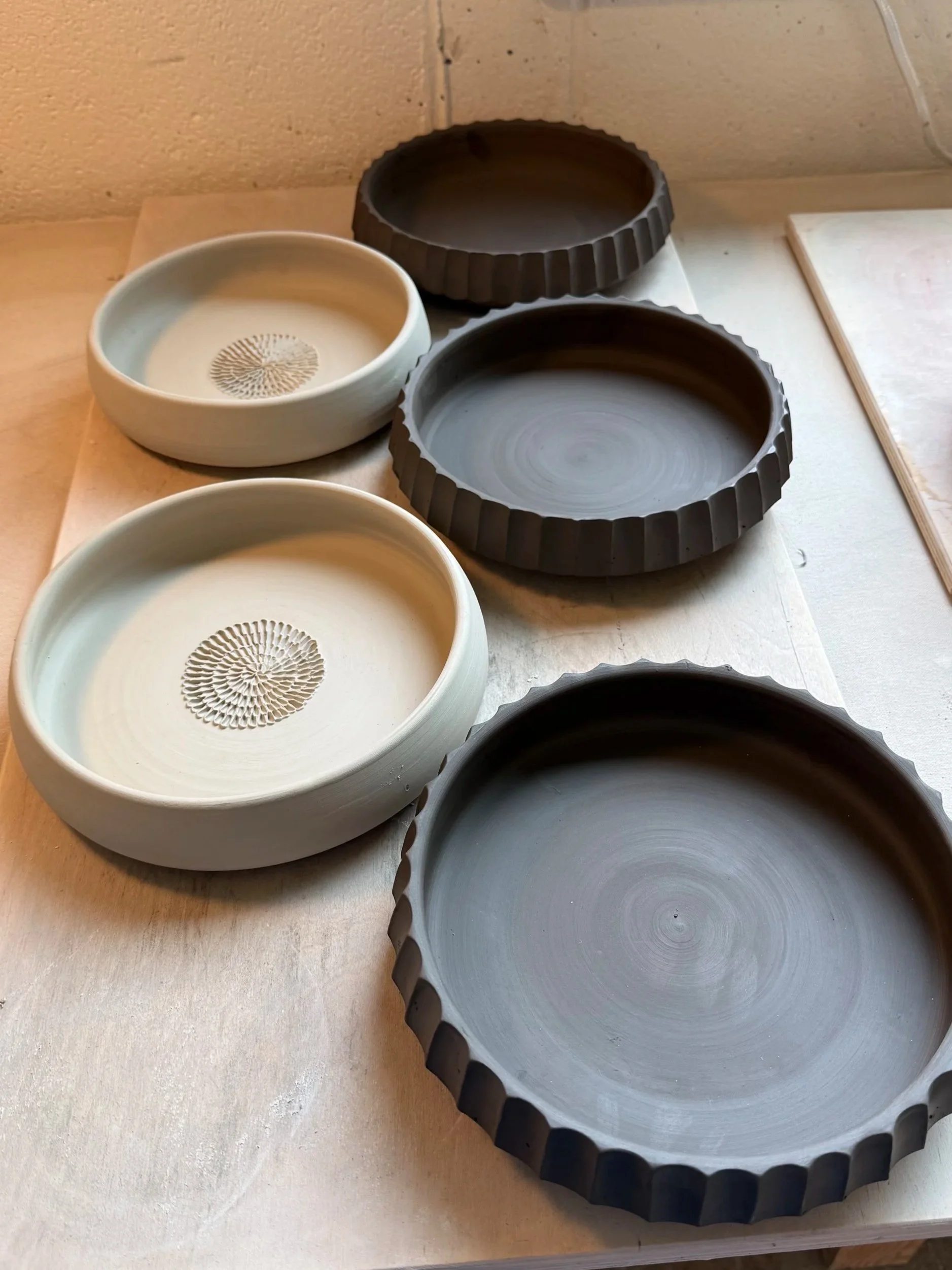 Several unfinished ceramic bowls and fluted ring molds on a wooden table in a ceramics studio.