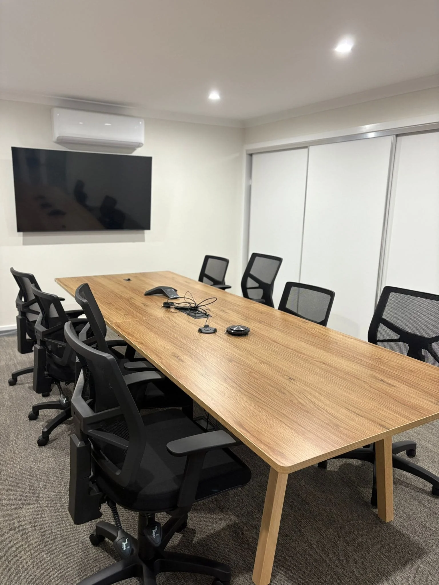 Commercial boardroom with a long timber meeting table, black mesh chairs and a wall-mounted screen, part of the Nolan St fit-out in Bendigo.