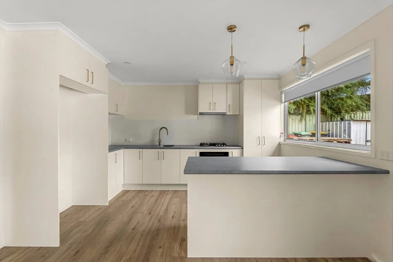 Renovated kitchen with cream shaker cabinetry, stone benchtops, brass tapware and glass pendant lights at the Hargreaves St renovation in Bendigo.