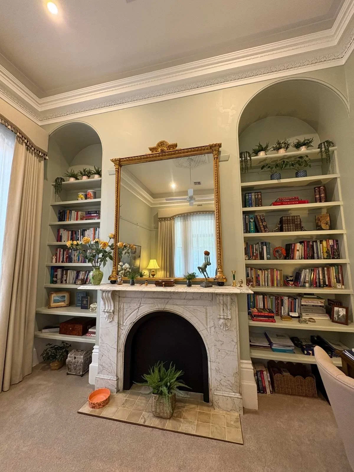 Home library with a marble fireplace, gilt mirror and arched built-in bookshelves in the Barkly St heritage home in Bendigo by AMW Builders.
