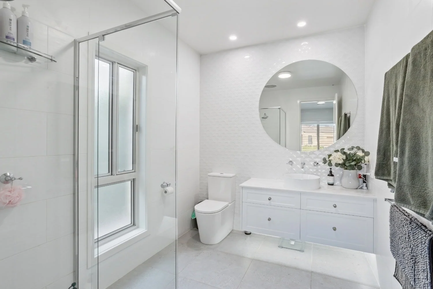 Main bathroom with a white vanity, vessel basin, round mirror and scalloped feature tiles beside a glass walk-in shower, finished in the Marnie Rd custom home in Bendigo by AMW Builders.
