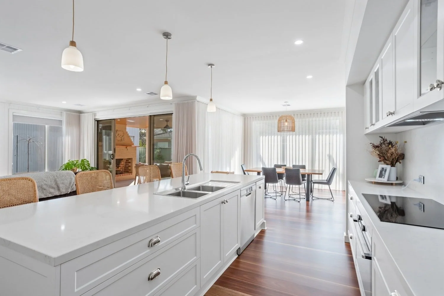 View along the white stone island and double sink toward the living zone, the alfresco sliding doors and the rear dining area in this open-plan Marnie Rd custom build by AMW Builders in Bendigo.