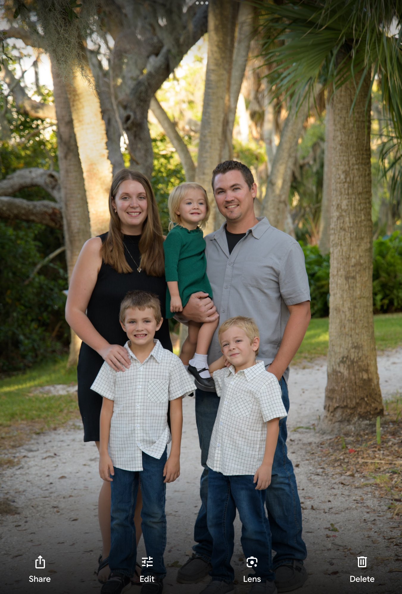 A family of six smiling outdoors surrounded by trees, with two adults, two girls, and two boys, posing for a photo.