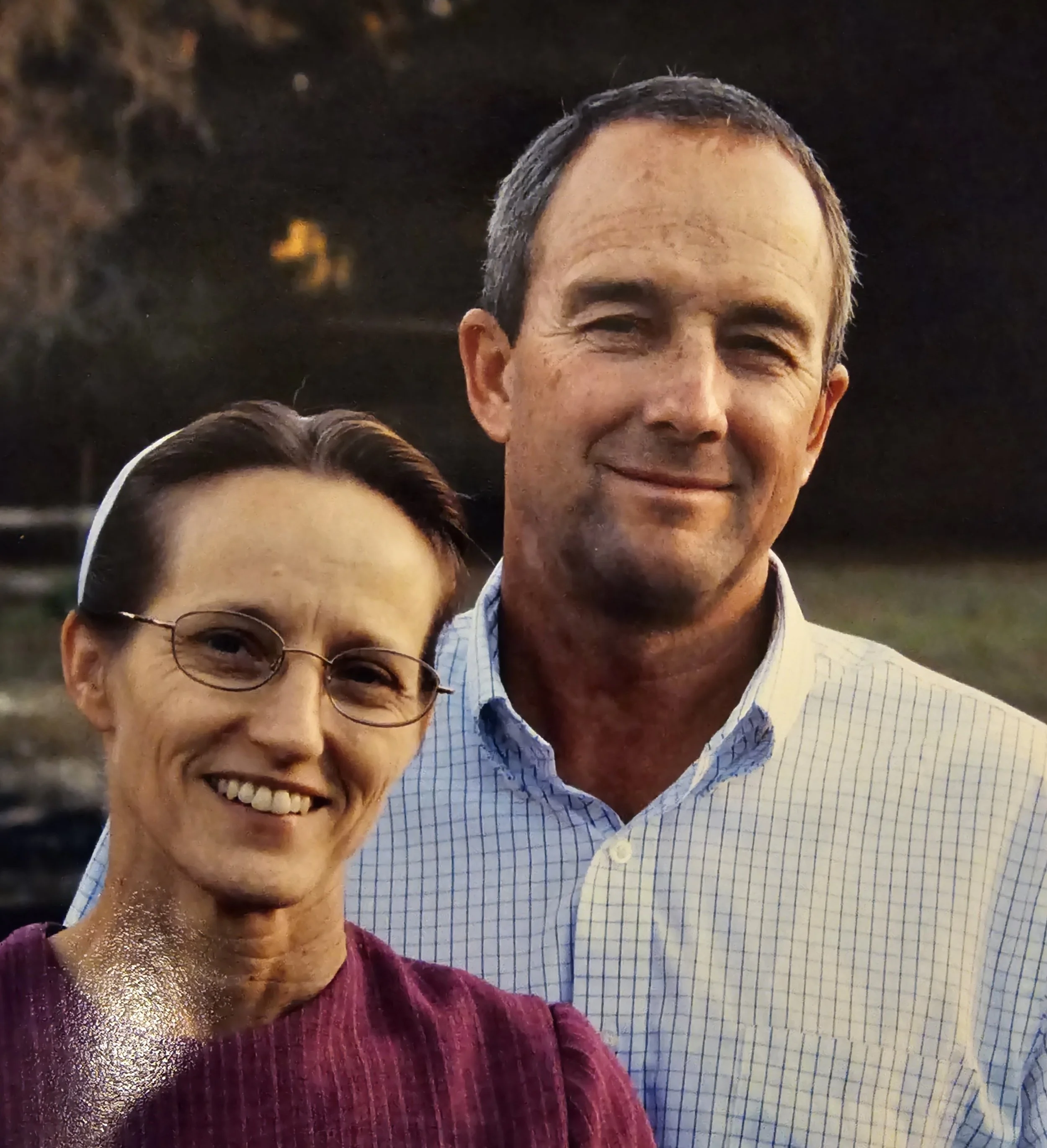 A smiling middle-aged man and woman standing close together outdoors during sunset.