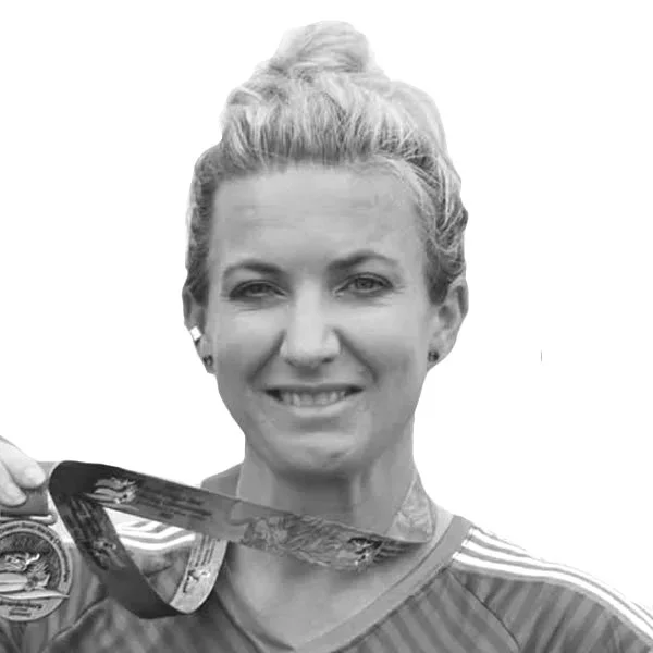 A woman with red hair wearing a blue hoodie and a lei of multicolored carnations, standing outdoors near water.