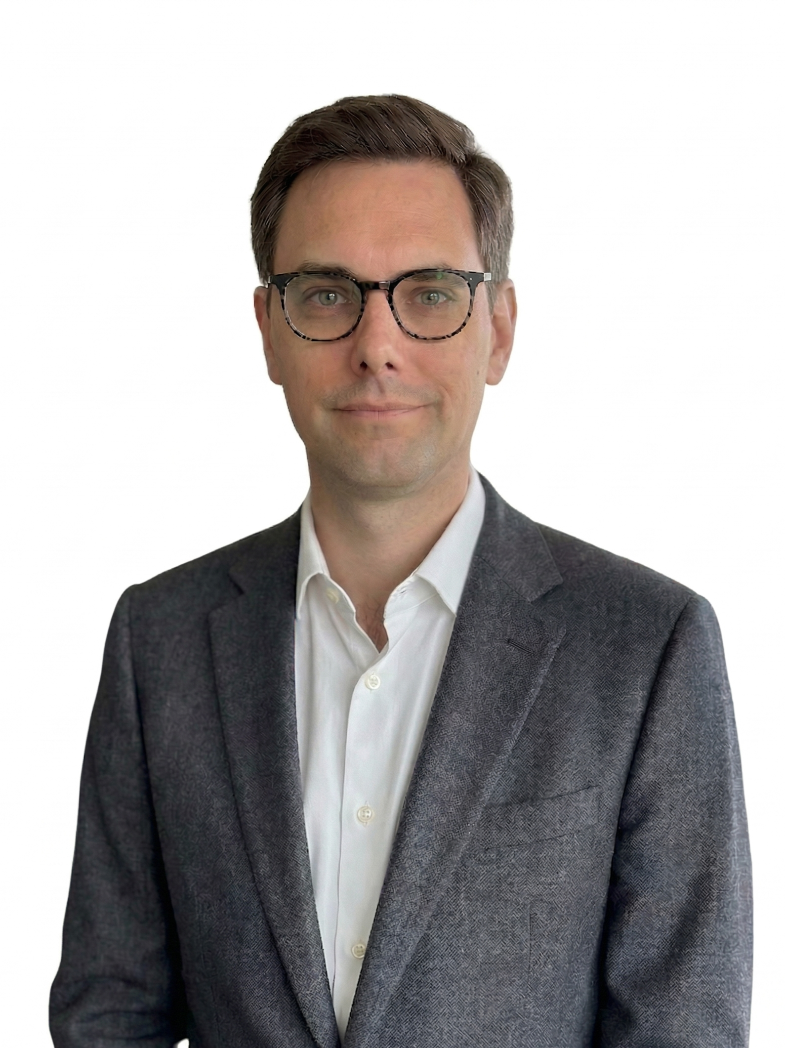 Portrait of a young man with brown hair, glasses, wearing a blue shirt and tan blazer, smiling against a white background.