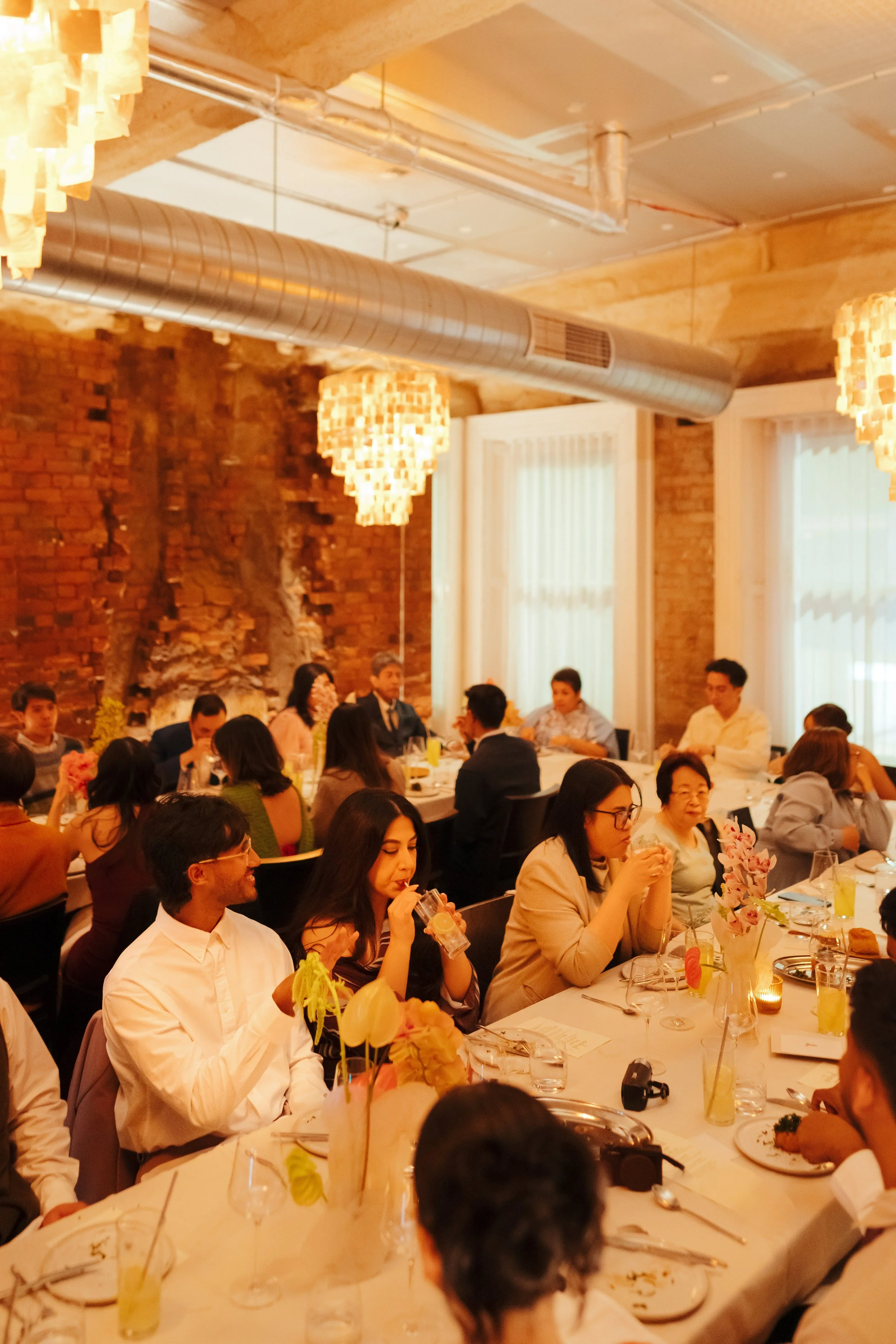 Askal's private dining room for wedding reception. People sitting around a dining table at a social event or dinner party in a warmly lit room with exposed brick walls and hanging lamps.