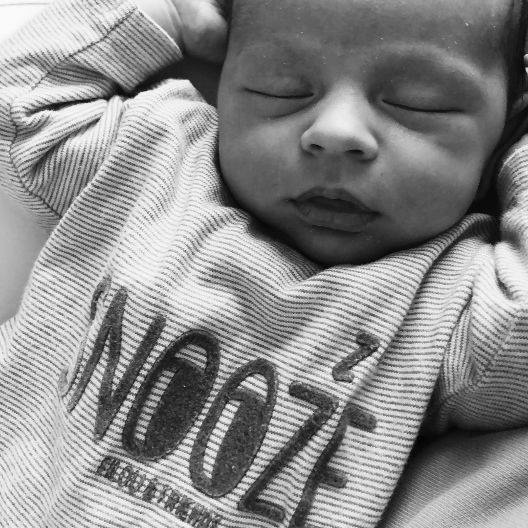Black and white photo of a sleeping baby wearing a striped shirt with the word 'SNOOZE' printed on it.