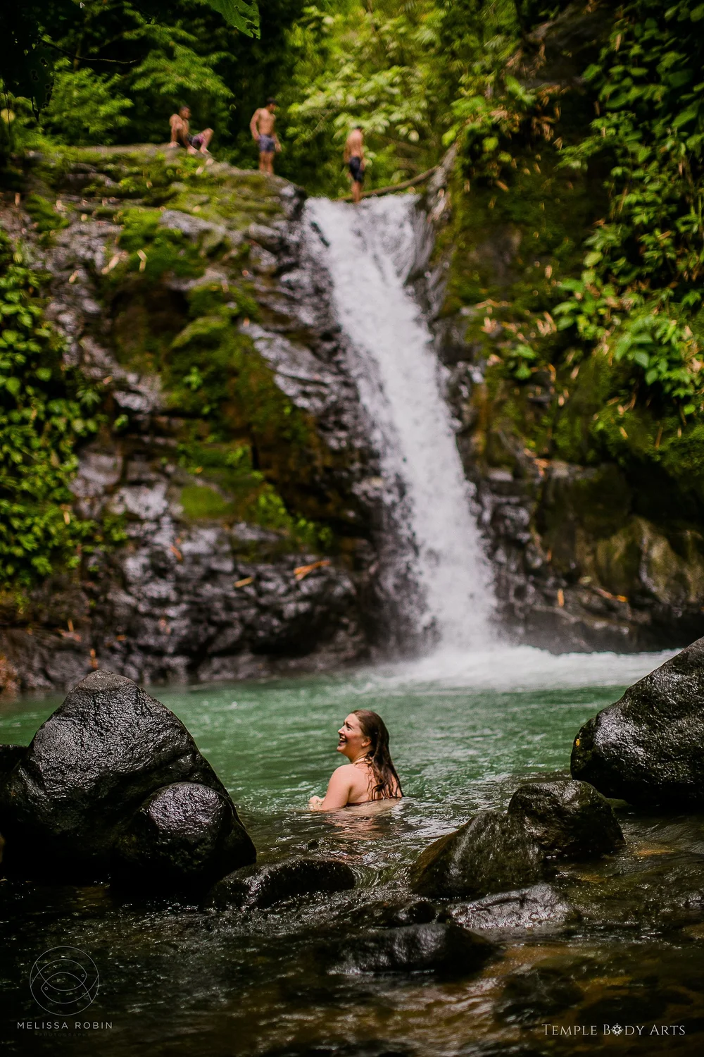 A woman standing beneath a jungle waterfall