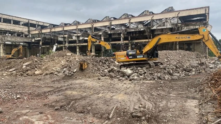 Maquinaria de construcción trabajando en un sitio de demolición o remoción de tierra frente a un edificio en ruinas