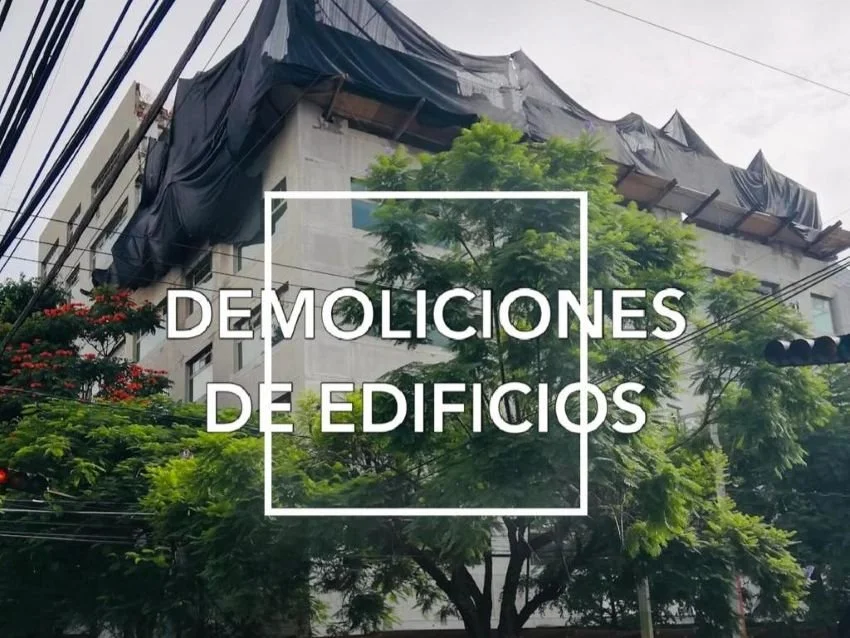 Edificio en proceso de demolición rodeado de árboles y cables eléctricos, con lona negra en el techo.