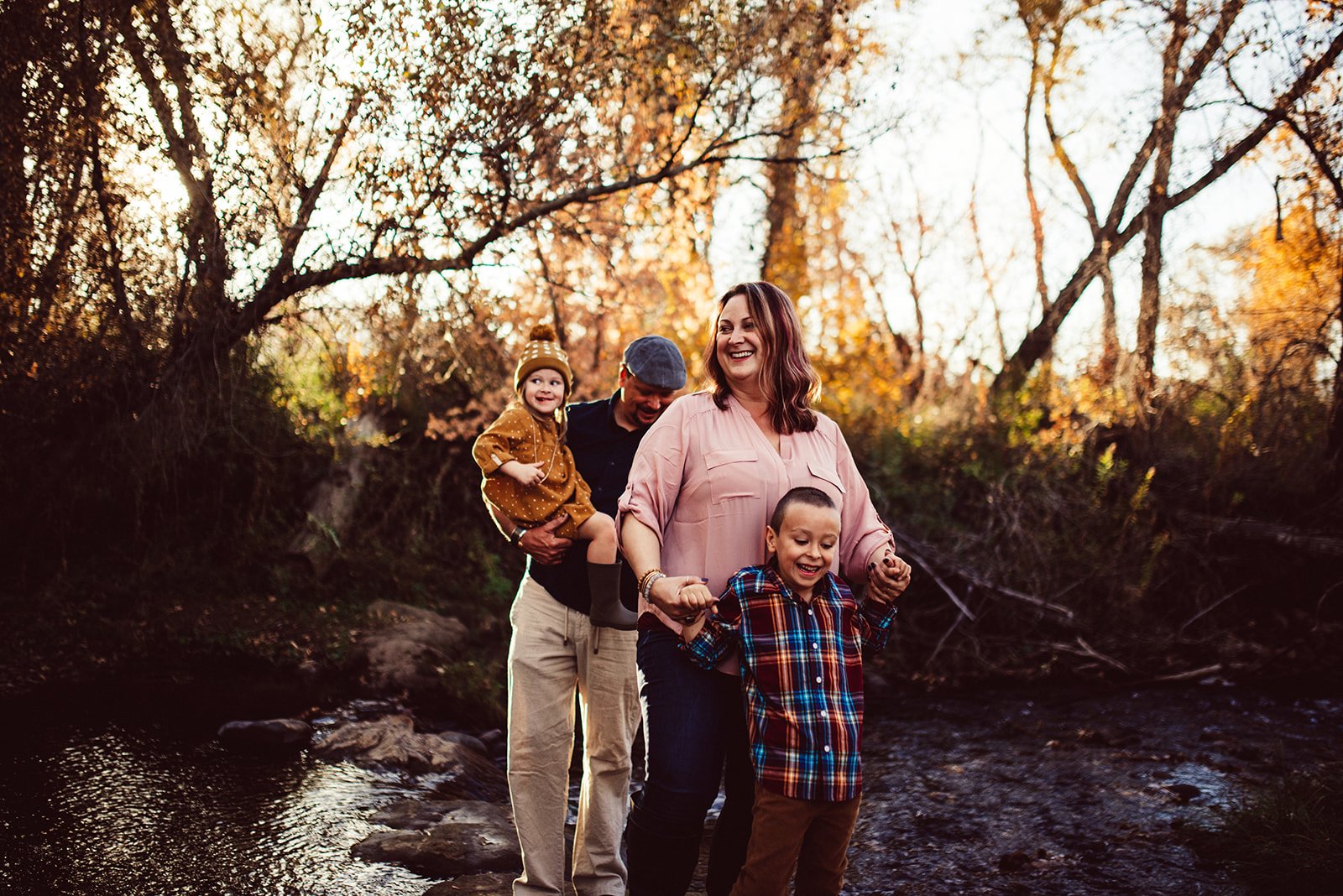 family of four smile together in golden forest