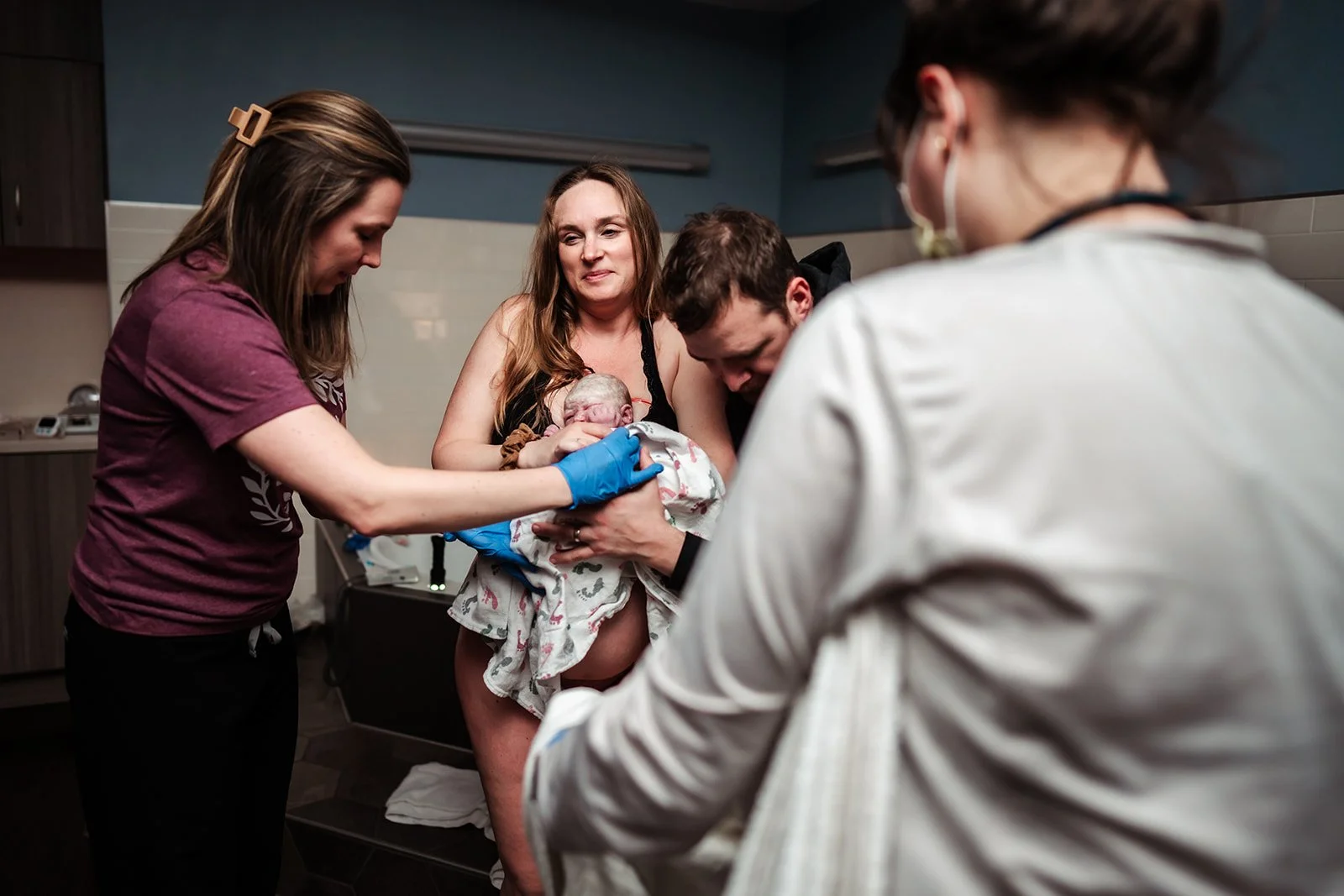 woman walking from bath to bed holding newborn being assisted by her midwife and partner