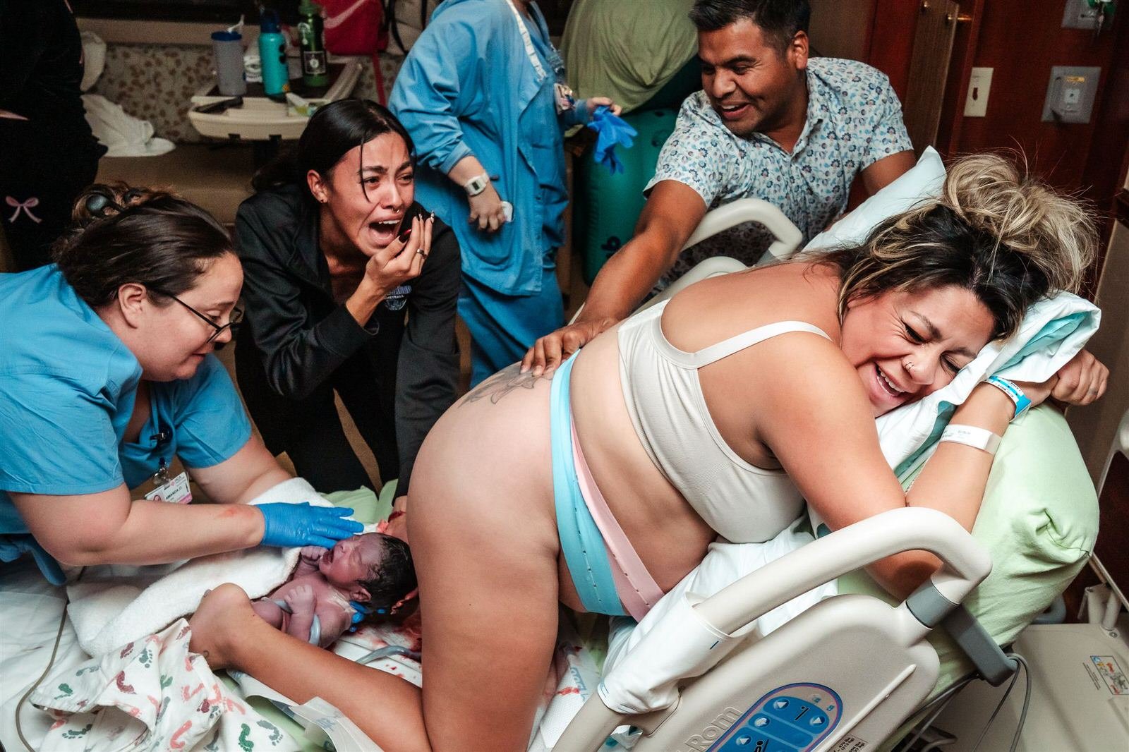 mother giving birth in the hospital on all fours on the bed,surround by family