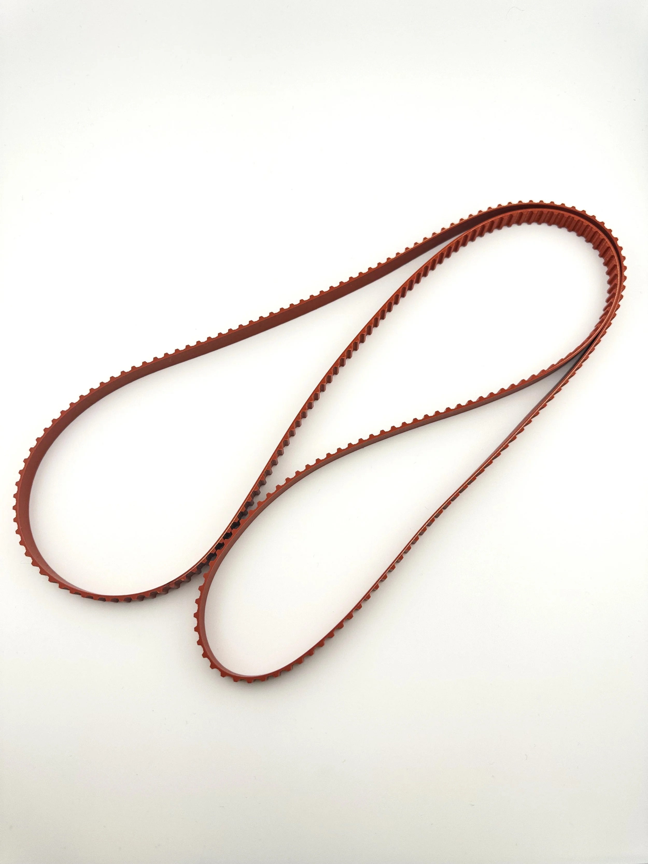 A red rubber timing belt for a car engine, laid out on a white surface.