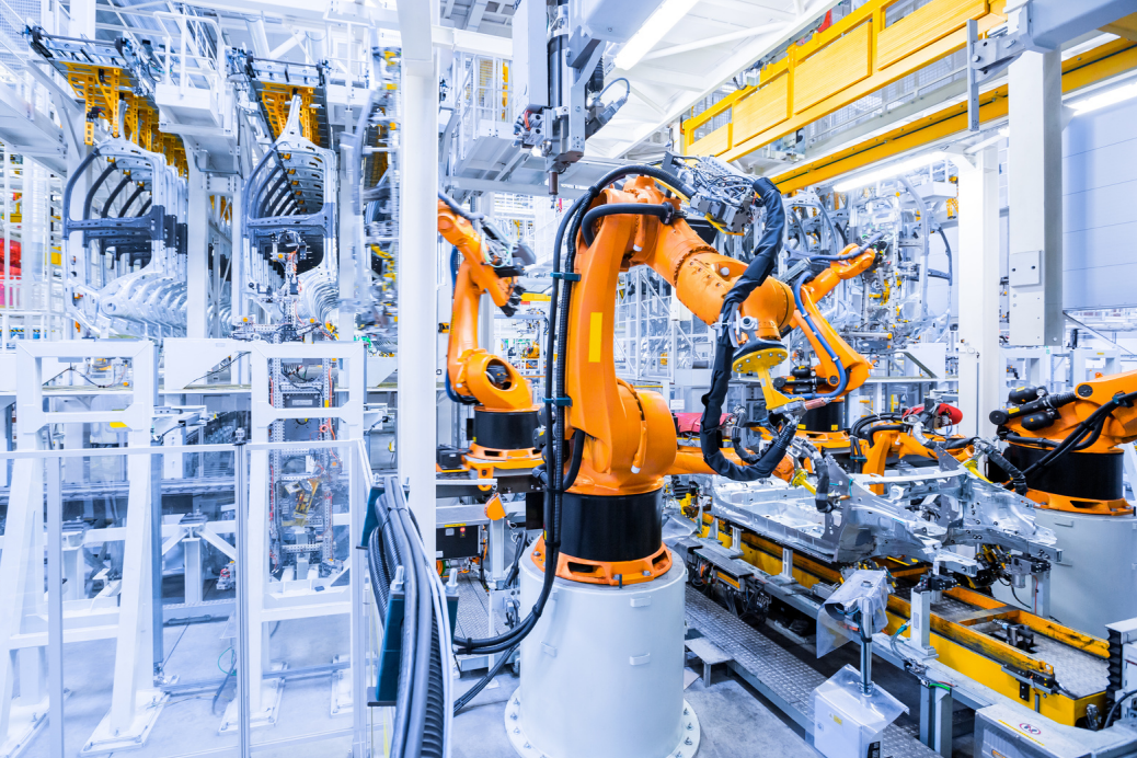 Industrial robotic arms assembling a vehicle frame on a production line in a clean, brightly lit factory.