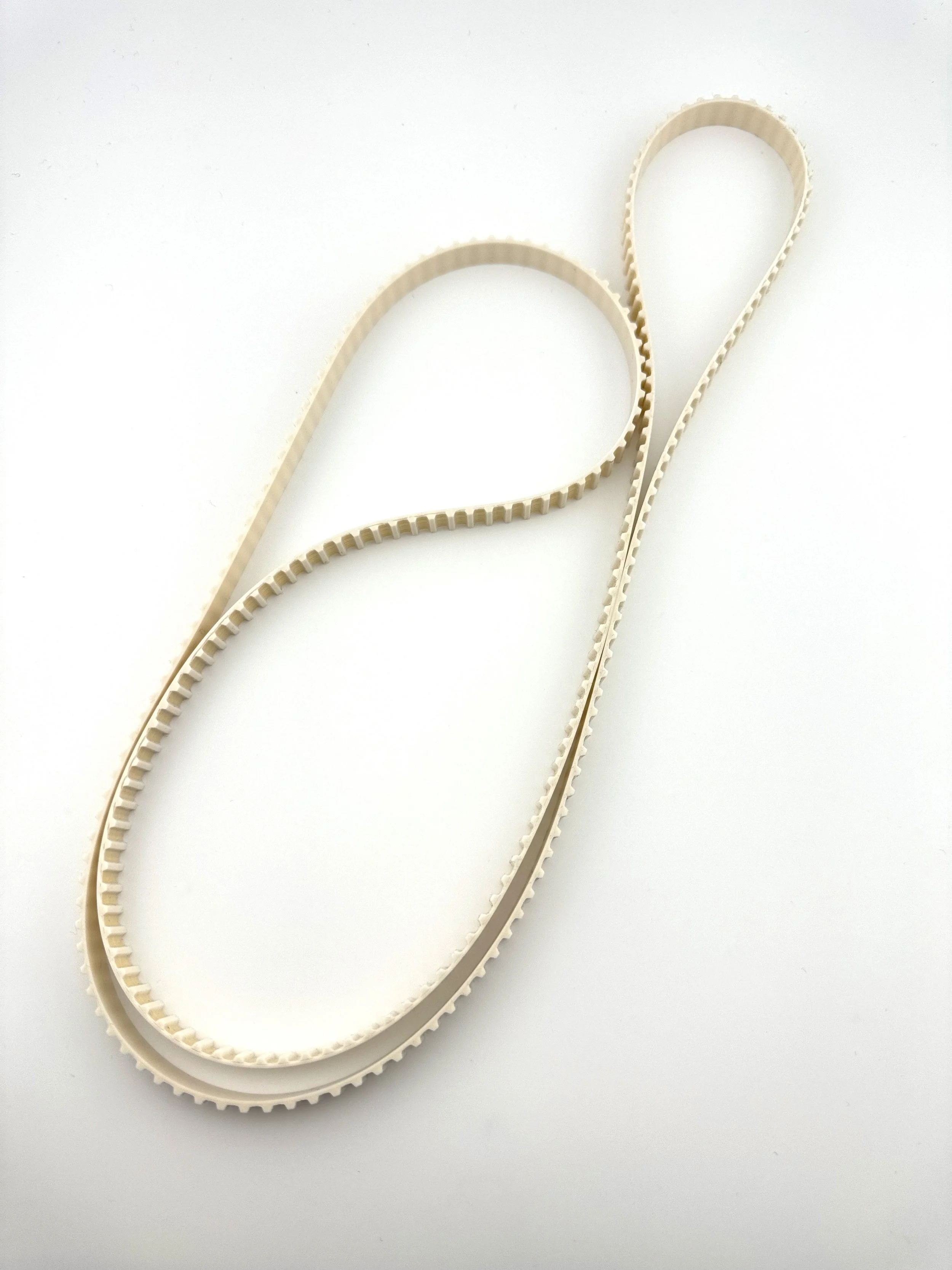 A beige plastic or rubber belt with evenly spaced teeth on its inner side, laid out on a white surface.