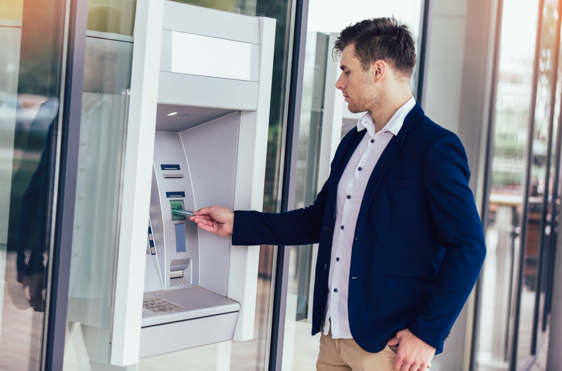 A man in business attire using an ATM machine outside a building.