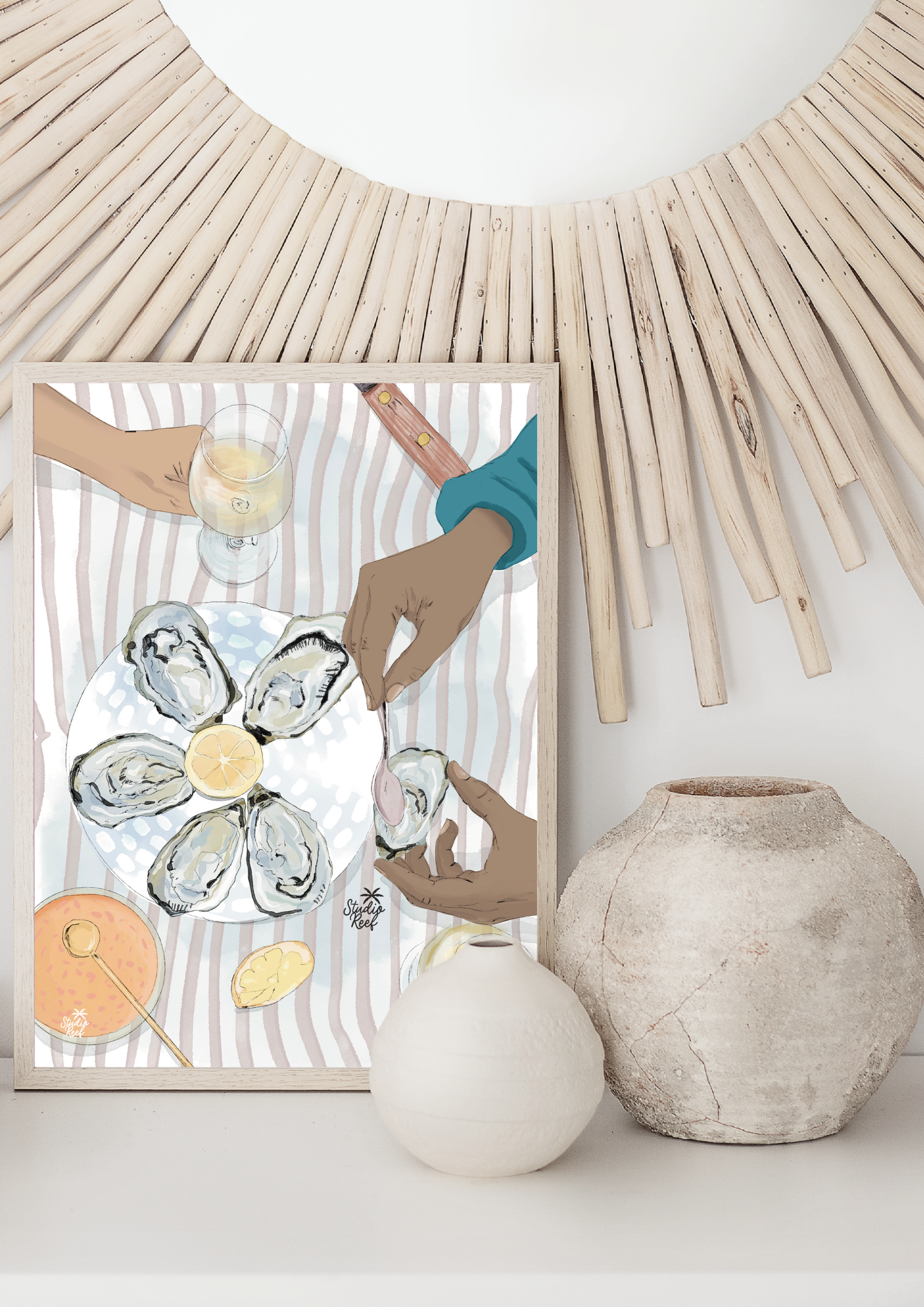 Une illustration d'une personne mangeant des huîtres avec un citron, à côté d'un verre de vin blanc, sur une nappe rayée. La illustration est encadrée et est posée sur une surface avec deux vases en dessous, un blanc avec une texture lisse et un autr